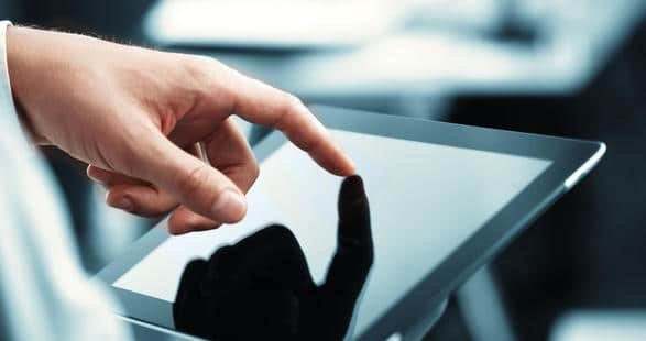 Une main pointe vers une tablette affichant des applications.